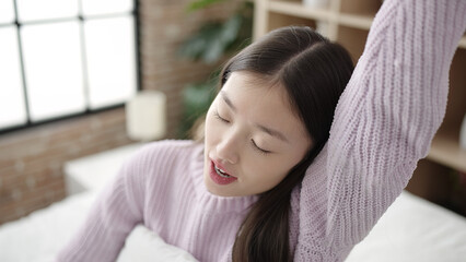 Young chinese woman waking up stretching arms at bedroom