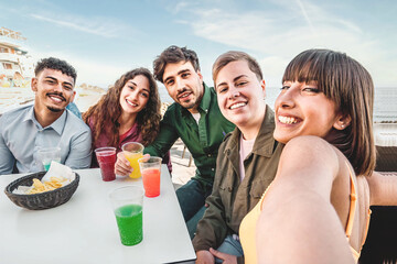 Diverse Friends Taking Selfie at Outdoor Bar - A multiracial group takes a selfie at an outdoor bar table, with colorful drinks on the table, all smiling.
