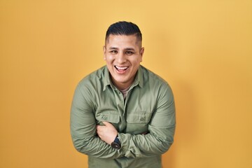 Hispanic young man standing over yellow background smiling and laughing hard out loud because funny crazy joke with hands on body.