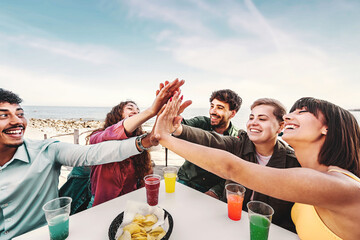 Multiracial Friends High-Five at Outdoor Bar - Diverse friends celebrate with a high-five, sea and sky in the background, shot with wide-angle lens, space for text.