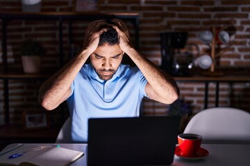 Hispanic man with beard using laptop at night suffering from headache desperate and stressed because pain and migraine. hands on head.