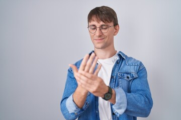 Caucasian blond man standing wearing glasses suffering pain on hands and fingers, arthritis...