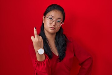 Asian young woman standing over red background showing middle finger, impolite and rude fuck off...