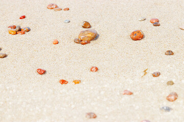 Natural stones amber yellow colored on beige sand. Aesthetic minimal nature scene with pebble stones on fine sandy background. Summer vacation or relaxation concept, selective focus
