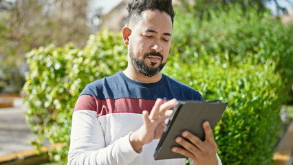 Fototapeta premium Young latin man using touchpad at park