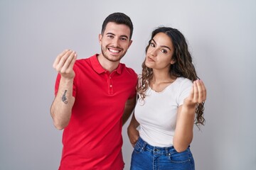 Young hispanic couple standing over isolated background doing italian gesture with hand and fingers confident expression