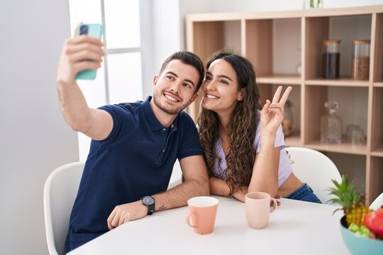 Young hispanic couple drinking coffee and make selfie by smartphone at home