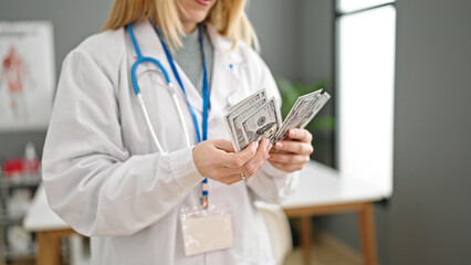 Young blonde woman doctor counting dollars at clinic