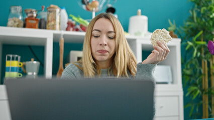 Young blonde woman using laptop eating rice cake at dinning room