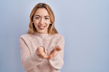Hispanic woman standing over blue background smiling with hands palms together receiving or giving...