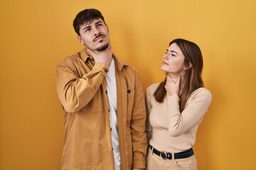 Young hispanic couple standing over yellow background touching painful neck, sore throat for flu, clod and infection