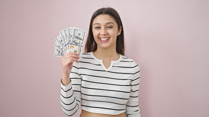 Young beautiful hispanic woman smiling confident holding dollars over isolated pink background