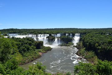 View of the Iguazu Falls hidden among the trees. Boats with tourists sail under the waterfall.