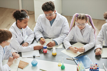 Top view at diverse group of children doing experiments during science class in school and wearing lab coats