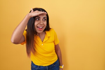 Young arab woman standing over yellow background very happy and smiling looking far away with hand over head. searching concept.