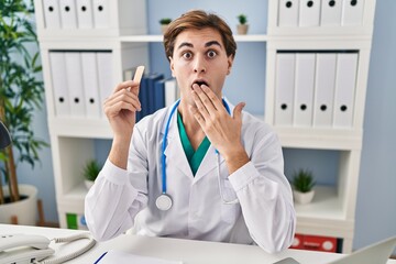 Young doctor man holding band aid covering mouth with hand, shocked and afraid for mistake....