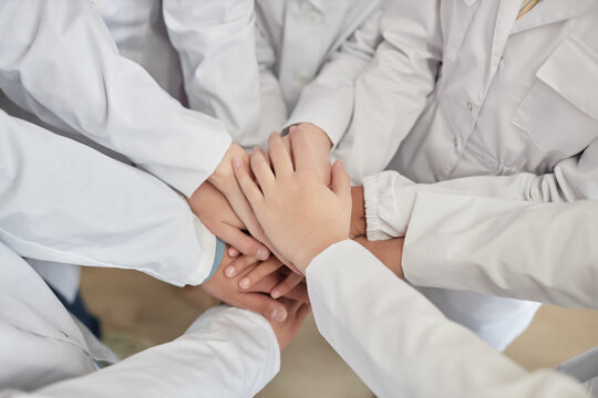 Top view closeup of group of children stacking hands in science class with white lab coats