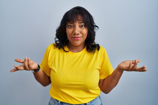 Hispanic woman standing over blue background clueless and confused with open arms, no idea concept.