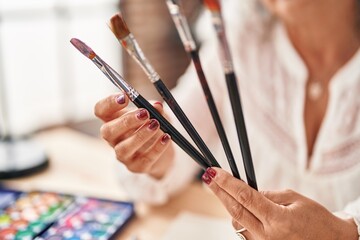 Middle age woman artist holding paintbrushes at art studio