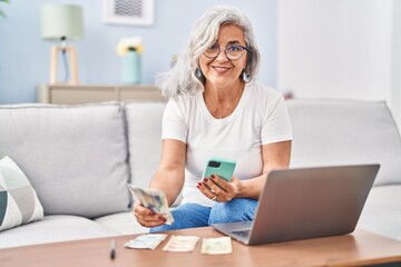 Middle age woman accounting using laptop and smartphone sitting on sofa at home