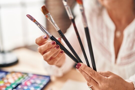 Middle age woman artist holding paintbrushes at art studio - Powered by Adobe