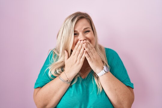 Caucasian plus size woman standing over pink background laughing and embarrassed giggle covering mouth with hands, gossip and scandal concept