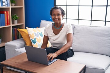 Middle age african american woman using laptop sitting on sofa at home