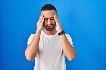 Fototapeta premium Young hispanic man standing over blue background with hand on head, headache because stress. suffering migraine.