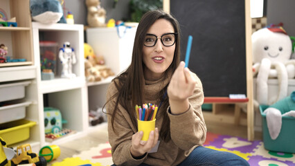 Beautiful hispanic woman preschool teacher smiling confident teaching color at kindergarten