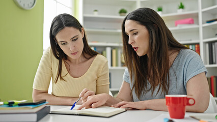 Two women reading book sitting on table at library university