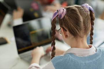 Back view at schoolgirl with cute pigtails using laptop in computer programming class for children, copy space