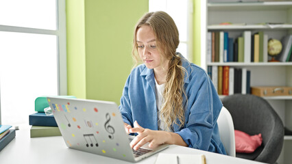 Young blonde woman student using laptop sitting on table at library university