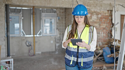 Young beautiful hispanic woman builder using touchpad at construction site