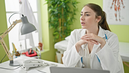 Young beautiful hispanic woman doctor sitting on table at clinic