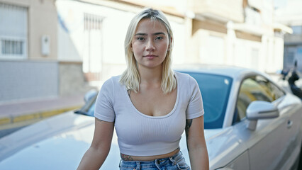 Young beautiful hispanic woman standing by car with serious expression at street