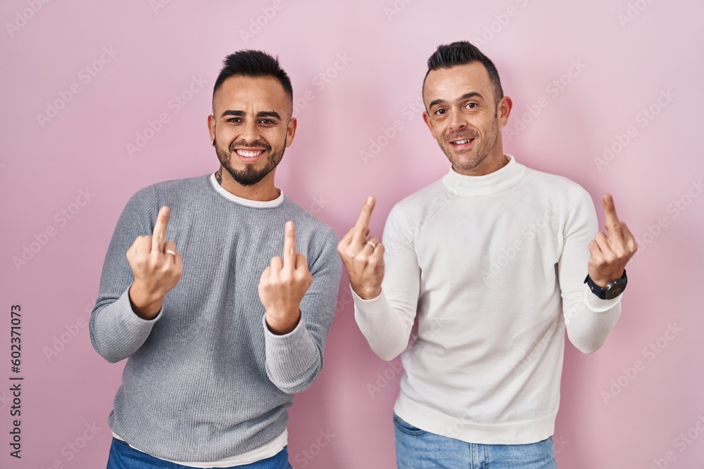 Poster Homosexual couple standing over pink background showing middle finger doing fuck you bad expression, provocation and rude attitude. screaming excited