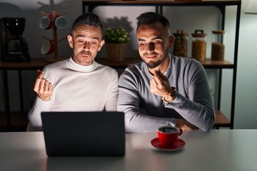 Homosexual couple using computer laptop doing money gesture with hands, asking for salary payment,...