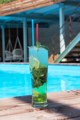 Mojito cocktail with lime and mint in highball glass at the swiming pool background on summer mountain background. Concept of summer relaxing