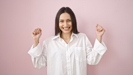 Young beautiful hispanic woman smiling confident standing with fists raised up over isolated pink...