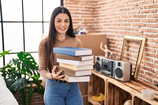 Young woman holding books at home smiling with a happy and cool smile on face. showing teeth.