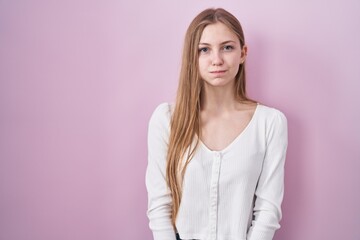 Young caucasian woman standing over pink background puffing cheeks with funny face. mouth inflated...