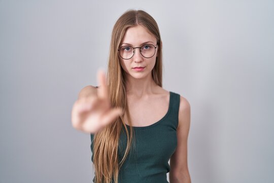 Young caucasian woman standing over white background pointing with finger up and angry expression, showing no gesture