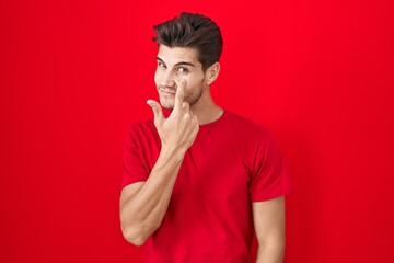 Young hispanic man standing over red background pointing to the eye watching you gesture, suspicious expression
