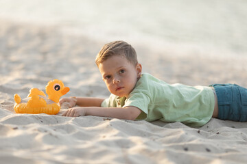 Little boy lying on a sandy beach at sunset.