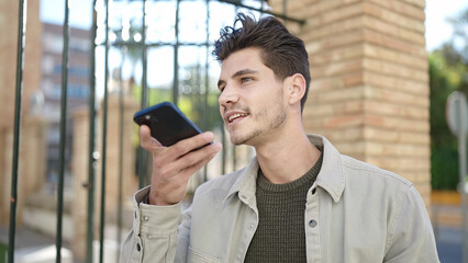 Young hispanic man smiling confident sending voice message by smartphone at street