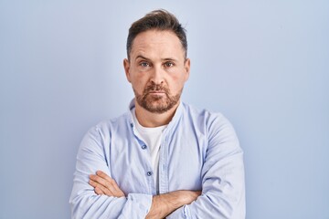 Middle age caucasian man standing over blue background skeptic and nervous, disapproving expression on face with crossed arms. negative person.
