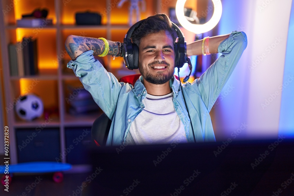 Sticker Young hispanic man streamer smiling confident relaxed with hands on head at gaming room