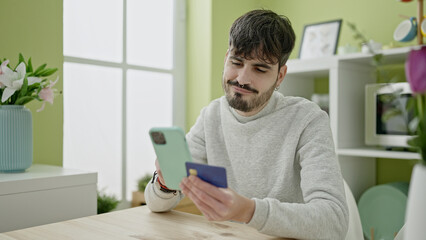 Young hispanic man shopping online with smartphone sitting on the table at dinning room