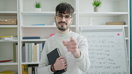 Young hispanic man teacher standing pointing to camera at university classroom