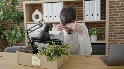 Fototapeta na wymiar Young hispanic man being fired packing belongings from workplace at office